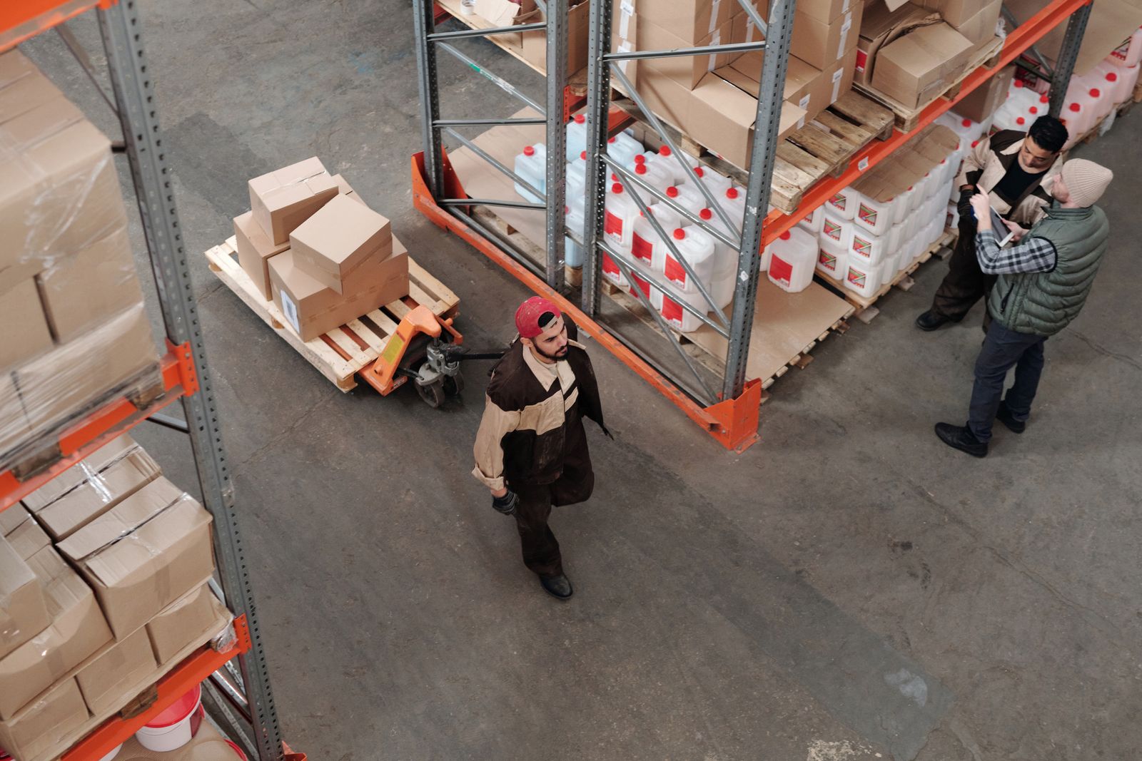 Warehouse aisle with palletized inventory and operators reviewing fulfillment status on a tablet