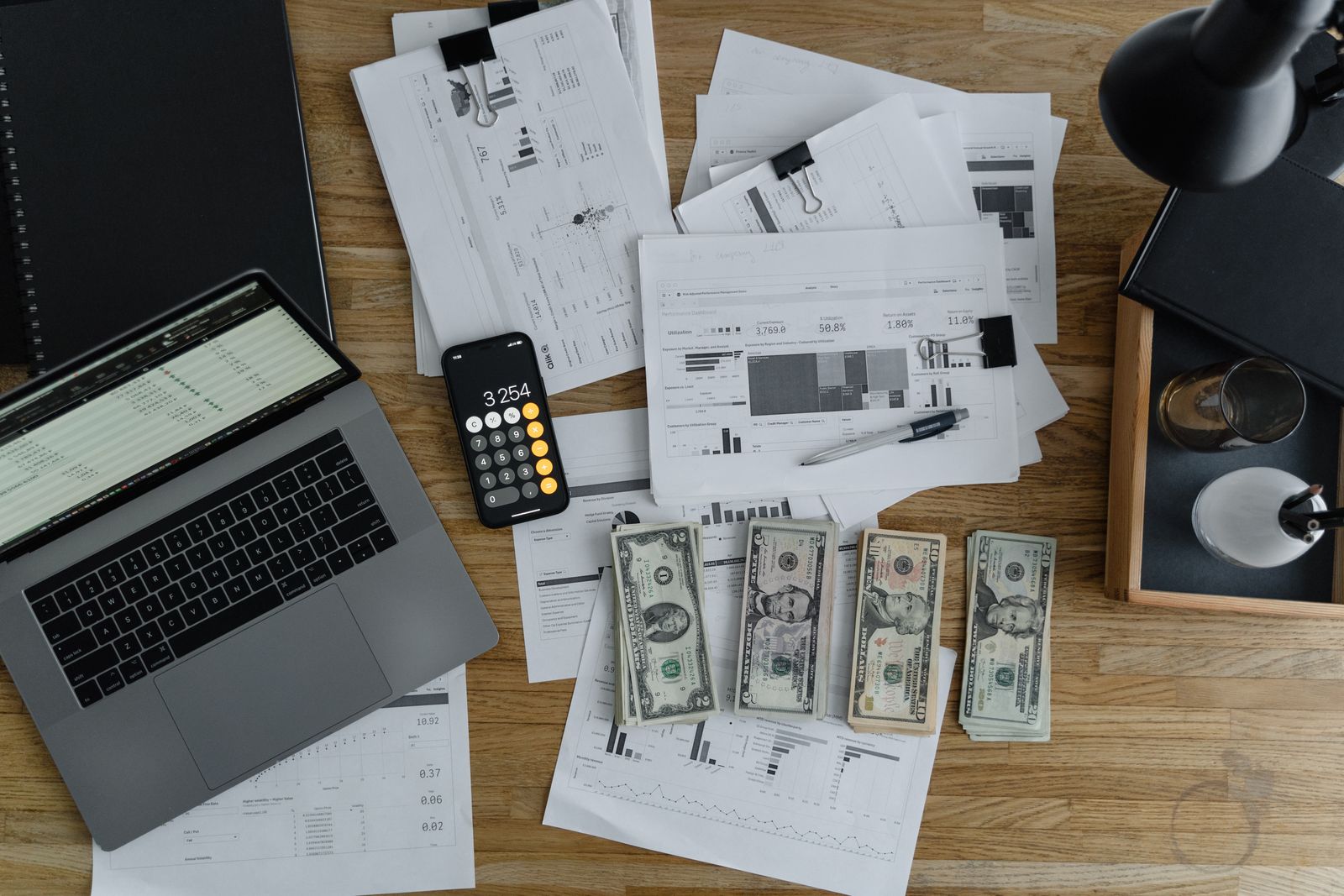 A finance operations desk with a laptop spreadsheet, calculator, printed reports, and payment records ready for reconciliation
